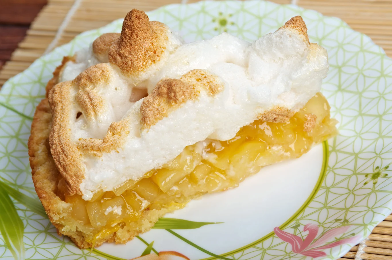 Szarlotka z lekką bezą i kwaskowymi jabłkami idealna na podwieczorek Kawałek szarlotki z bezą na złocistym spodzie z jabłkami, podany na ozdobnym talerzyku.