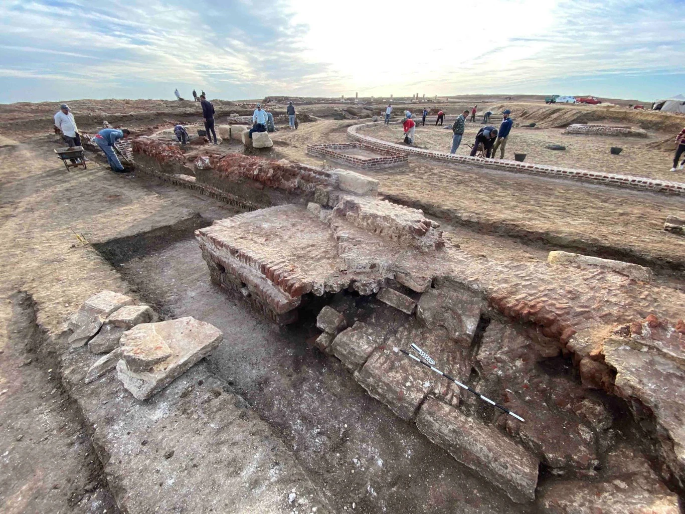 Odkryte fragmenty świątyni grupa archeologów pracująca przy wykopaliskach, odkrywająca fragmenty starych murów z cegły na rozległym, otwartym terenie, na pierwszym planie dobrze zachowane struktury fundamentów