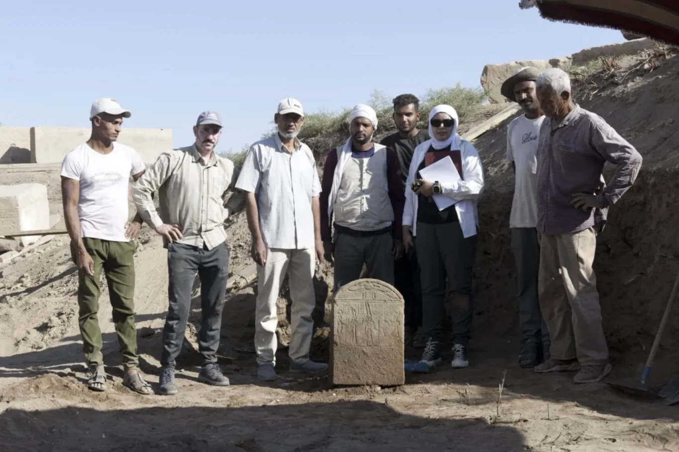 Stela sprzed 2000 lat odkryta w Luksorze. Cesarz Tyberiusz w roli faraona Stela cesarza Tyberiusza jako faraona odkryta przez archeologów w Luksorze, otoczona przez badaczy na wykopie.