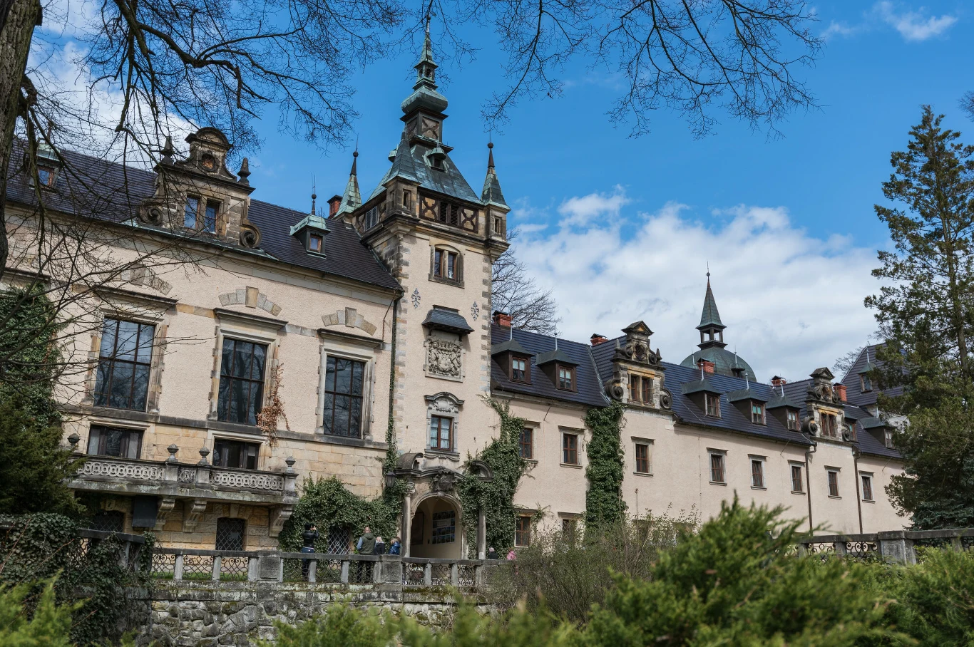 Zamek Kliczków to miejsce łączące przeszłość z nowoczesnością. Warto tam spędzić długi weekend majowy. Zamek Kliczków z jasną elewacją, ozdobnymi oknami i wieżyczkami, otoczony kamiennym murem oraz zielenią. Dolny Śląsk.