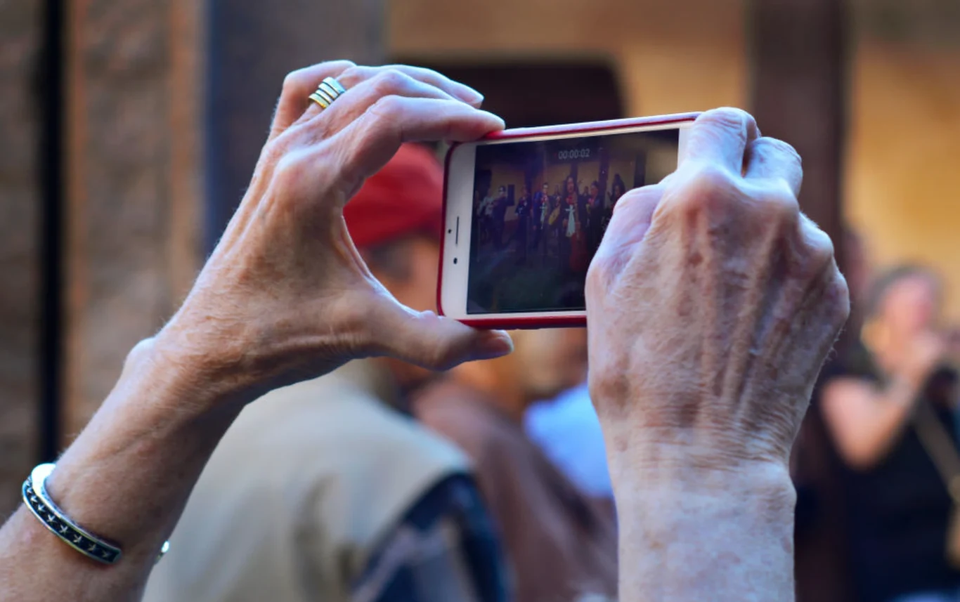 Seniorka w USA nie otworzyła drzwi policjantom. Gra wideo winowajcą Dłonie trzymające smartfon poziomo z widokiem grupy ludzi na ekranie; na palcu pierścionek i bransoletka.