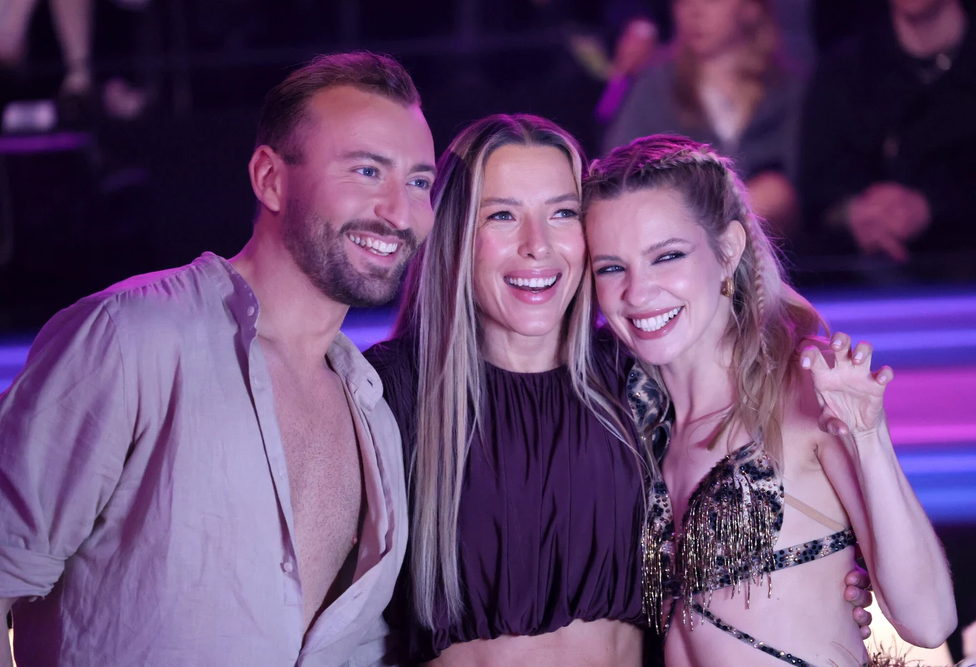 Michał Bartkiewicz, Ewa Chodakowska i Paulina Gałązka Trójka uśmiechniętych osób pozuje razem do zdjęcia na tle jasnych, kolorowych świateł, a atmosfera wydaje się radosna i przyjacielska.