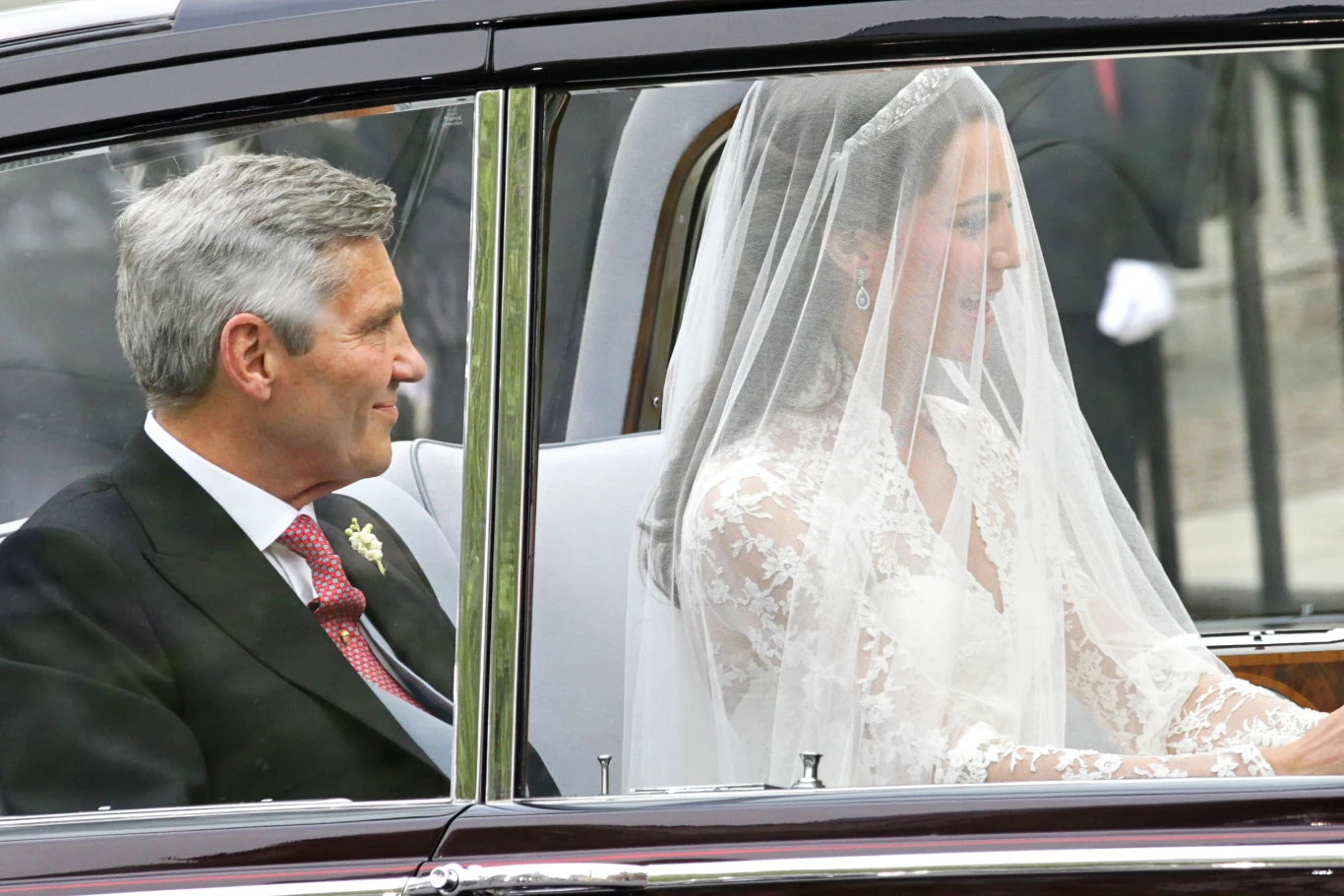Księżna Kate, Michael Middleton kobieta w białej, koronkowej sukni ślubnej i welonie siedzi w samochodzie obok starszego mężczyzny w garniturze z czerwonym krawatem i białą koszulą, oboje patrzą przed siebie