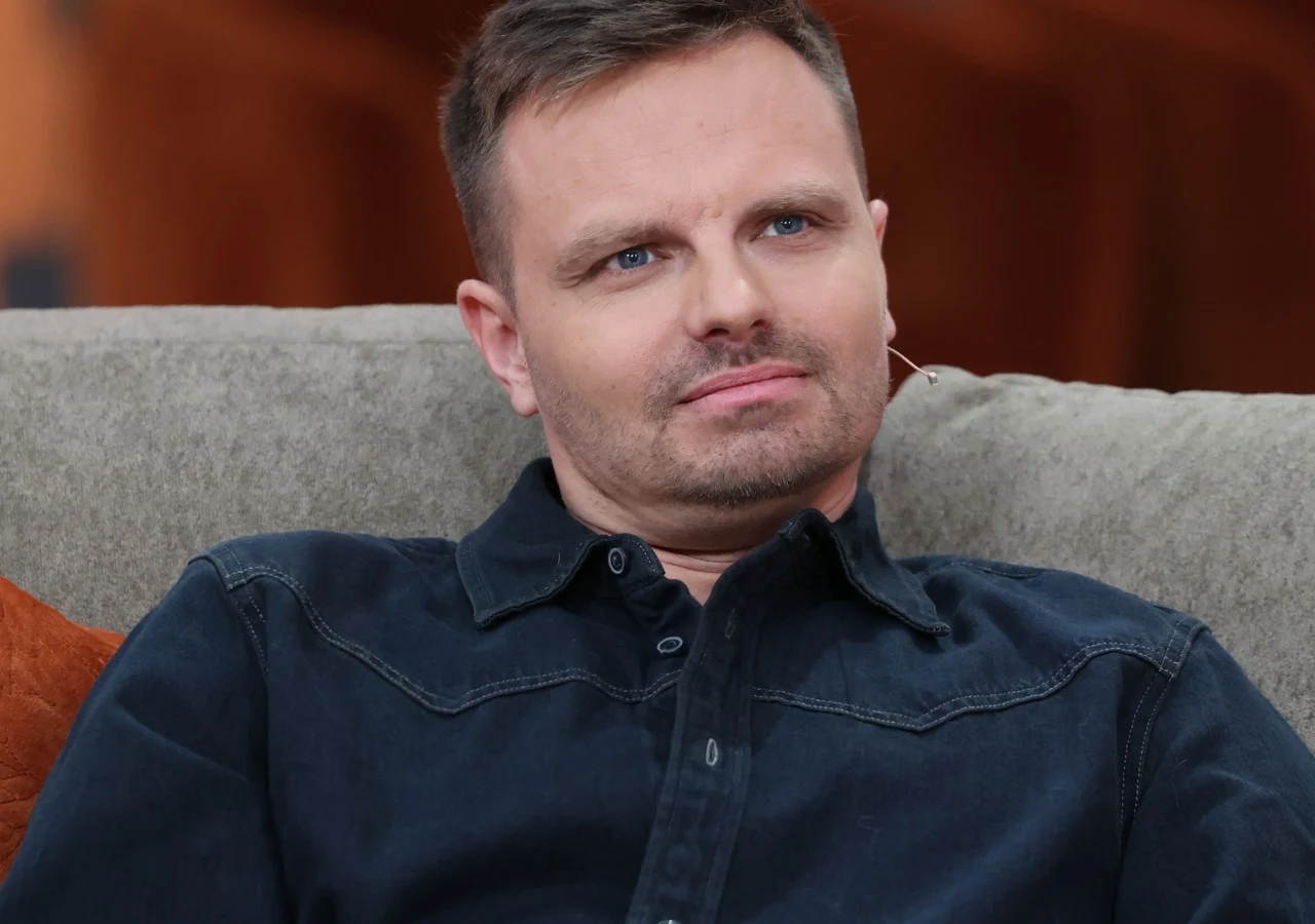 Marcin Hakiel Marcin Hakiel w ciemnej koszuli siedzi na szarej kanapie, z krótkimi włosami i lekkim uśmiechem.