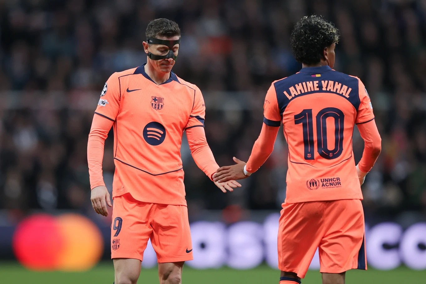 Robert Lewandowski i Lamine Yamal Robert Lewandowski i Lamine Yamal w różowych strojach FC Barcelony podczas meczu, Lewandowski podaje rękę Yamalowi.
