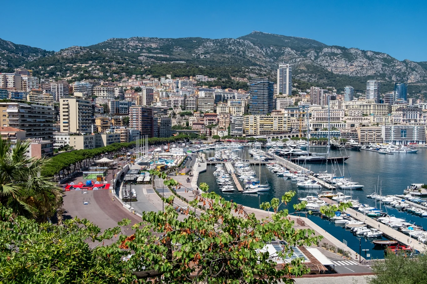 To drugie najmniejsze państwo świata. Dlaczego warto je odwiedzić? Port z luksusowymi jachtami w Monako, wysokie apartamentowce. W tle hotele, góry i zieleń.