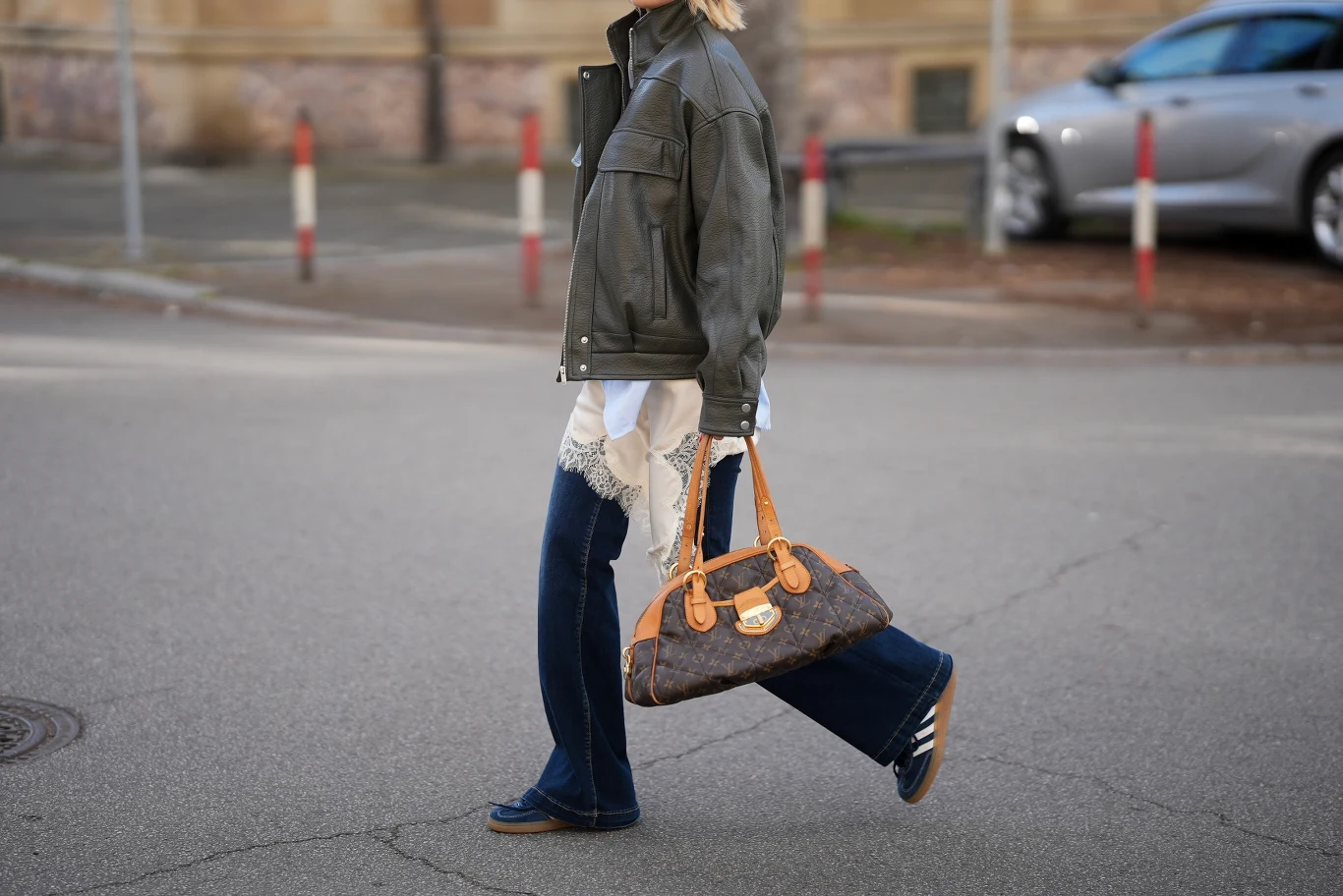 Jeansy typy flare i sportowe buty to wygodne i stylowe połączenie kobieta w ciemnej kurtce i niebieskich dżinsach przechodzi przez ulicę, trzymając w ręku dużą, brązową torebkę z elementami skórzanymi