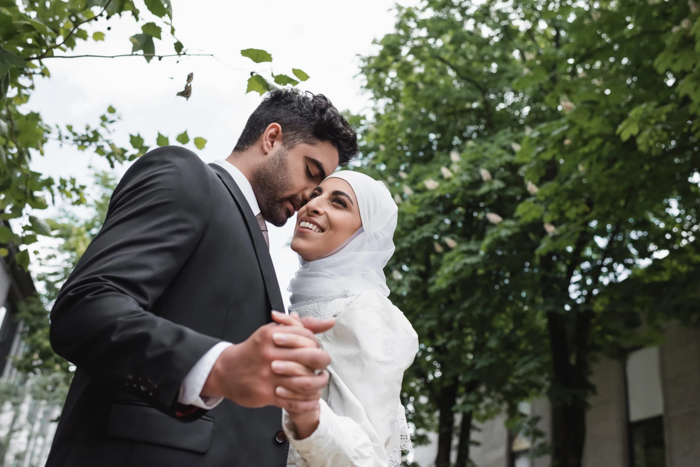 Młodzi ludzie z krajów arabskich często korzystają z pomocy rodziny, by znaleźć odpowiedniego partnera. Para młoda w eleganckich strojach trzyma się za ręce wśród zieleni podczas aranżowanego ślubu.