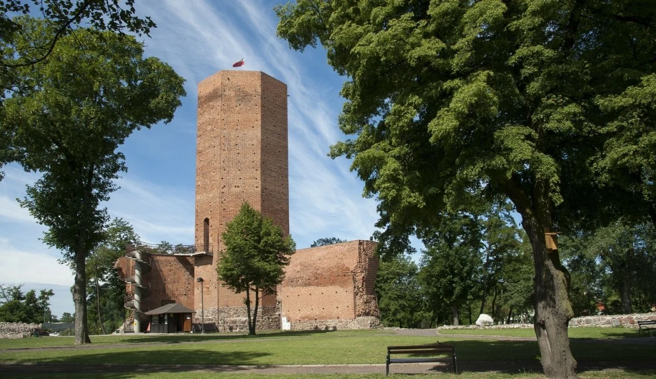 Mysia Wieża w Kruszwicy wiąże się z polską legendą o królu Popielu Mysia Wieża w Kruszwicy z czerwonej cegły, otoczona murami i drzewami, ławka na tle trawnika