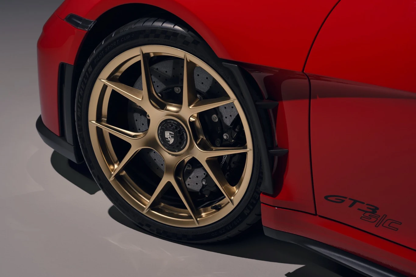 złota felga z logo Porsche na tle czerwonej karoserii samochodu sportowego, widoczny napis GT3 na drzwiach oraz duży wentylowany hamulec tarczowy