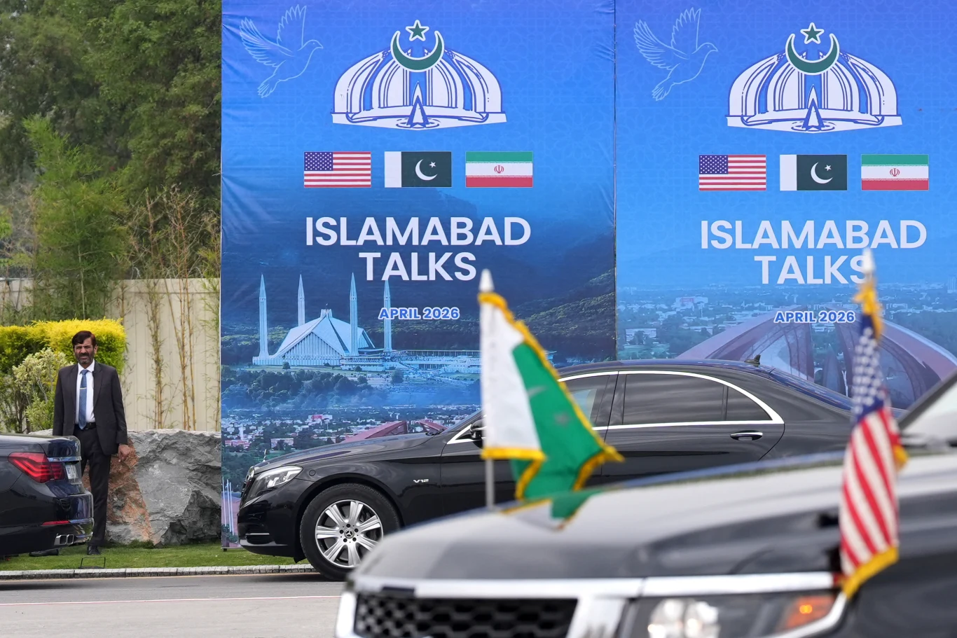Drugie podejście do rozmów pokojowych między USA i Iranem. Pakistan złożył propozycję Banery 'Islamabad Talks' z flagami USA, Pakistanu i Iranu, limuzyny rządowe, mężczyzna przy samochodzie.