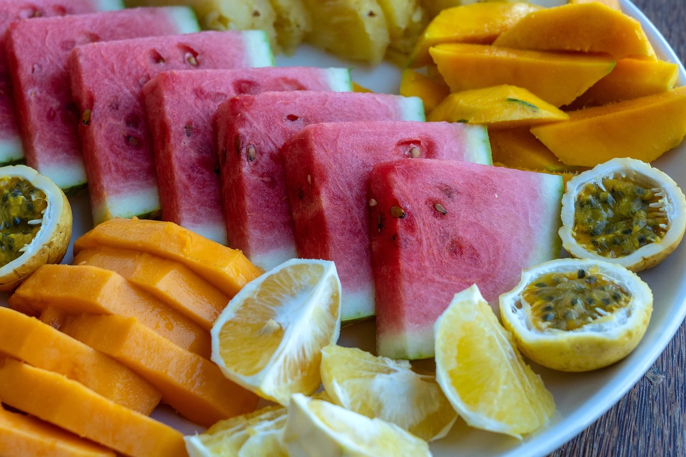 Owoce mogą być zdrowym urozmaiceniem diety, pod warunkiem, że są spożywanie w formie nieprzetworzonej Pokrojone kawałki arbuza, mango, papai, ananasa oraz połówki marakui i cytryny ułożone ciasno na białym talerzu, tworząc kolorową, apetyczną kompozycję tropikalnych owoców.