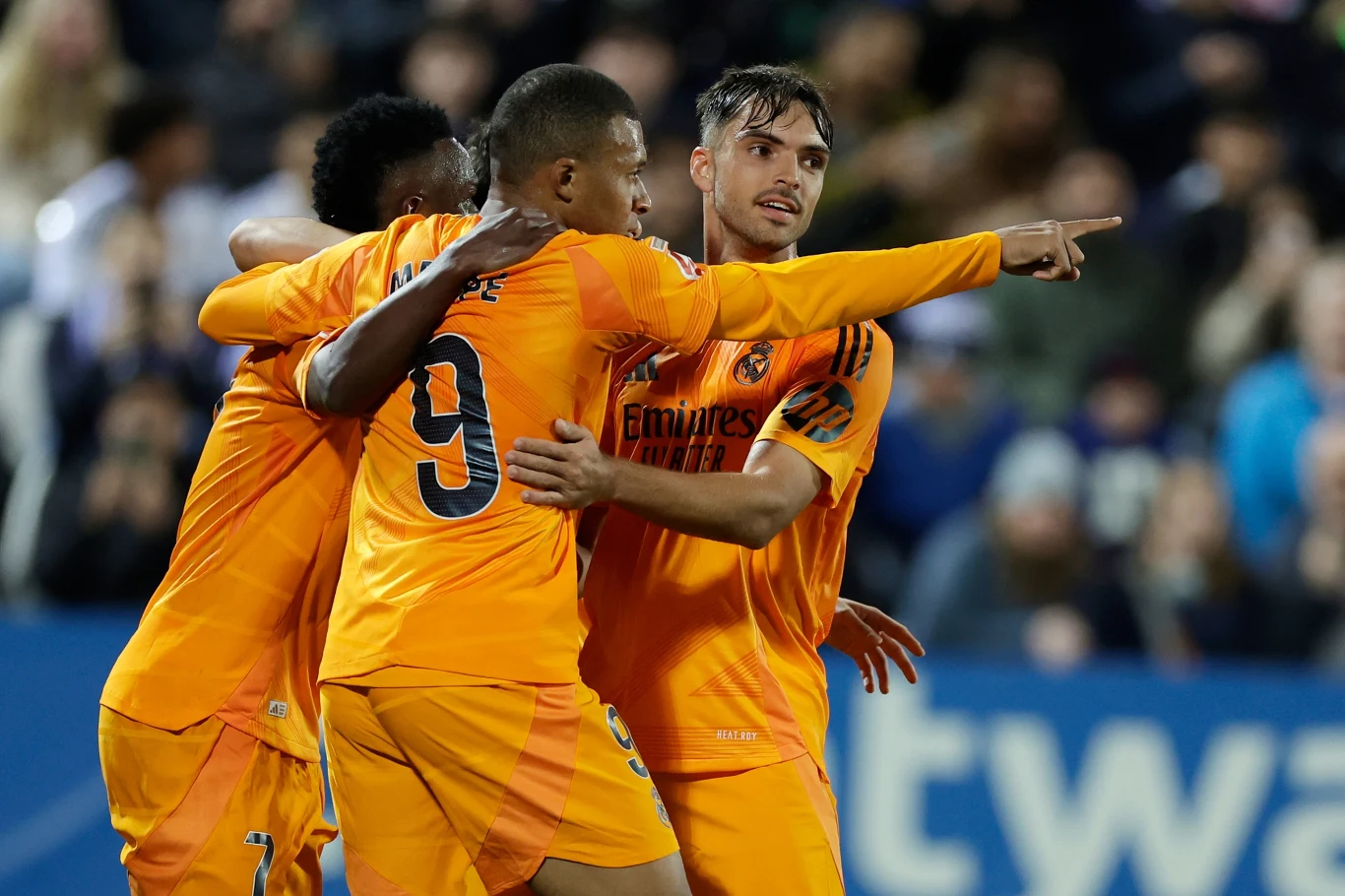 Vinicius Junior, Kylian Mbappe, Raul Asencio Vinicius Junior, Kylian Mbappe i Raul Asencio w pomarańczowych strojach Realu Madryt świętują gola na stadionie.