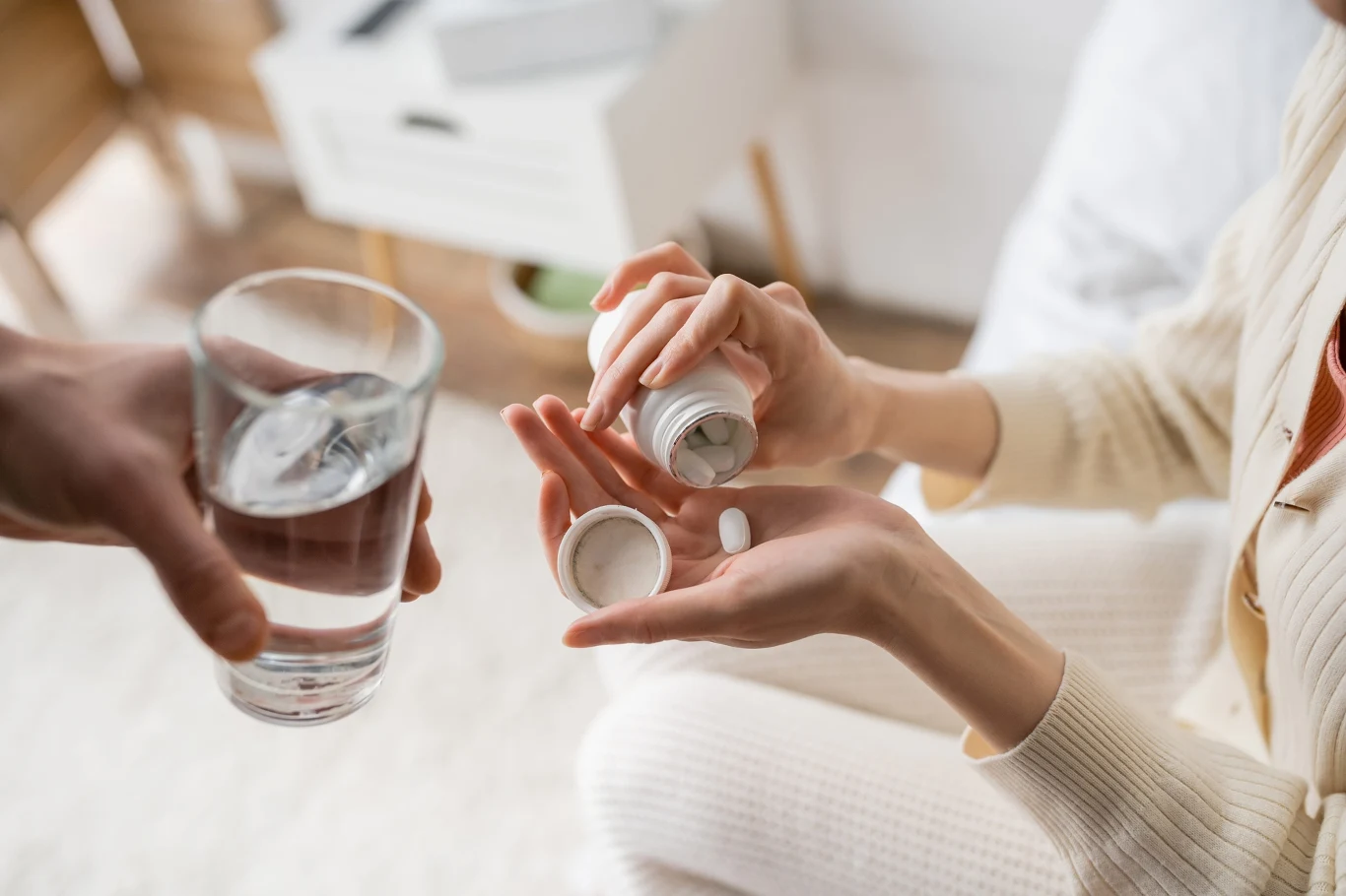 Witamina B10 wspiera układ nerwowy i bierze udział w produkcji serotoniny oraz dopaminy, które wpływają na nastrój osoba trzymająca w jednej dłoni otwarte opakowanie tabletek i wysypująca jedną do drugiej dłoni, naprzeciwko druga osoba podaje szklankę wody