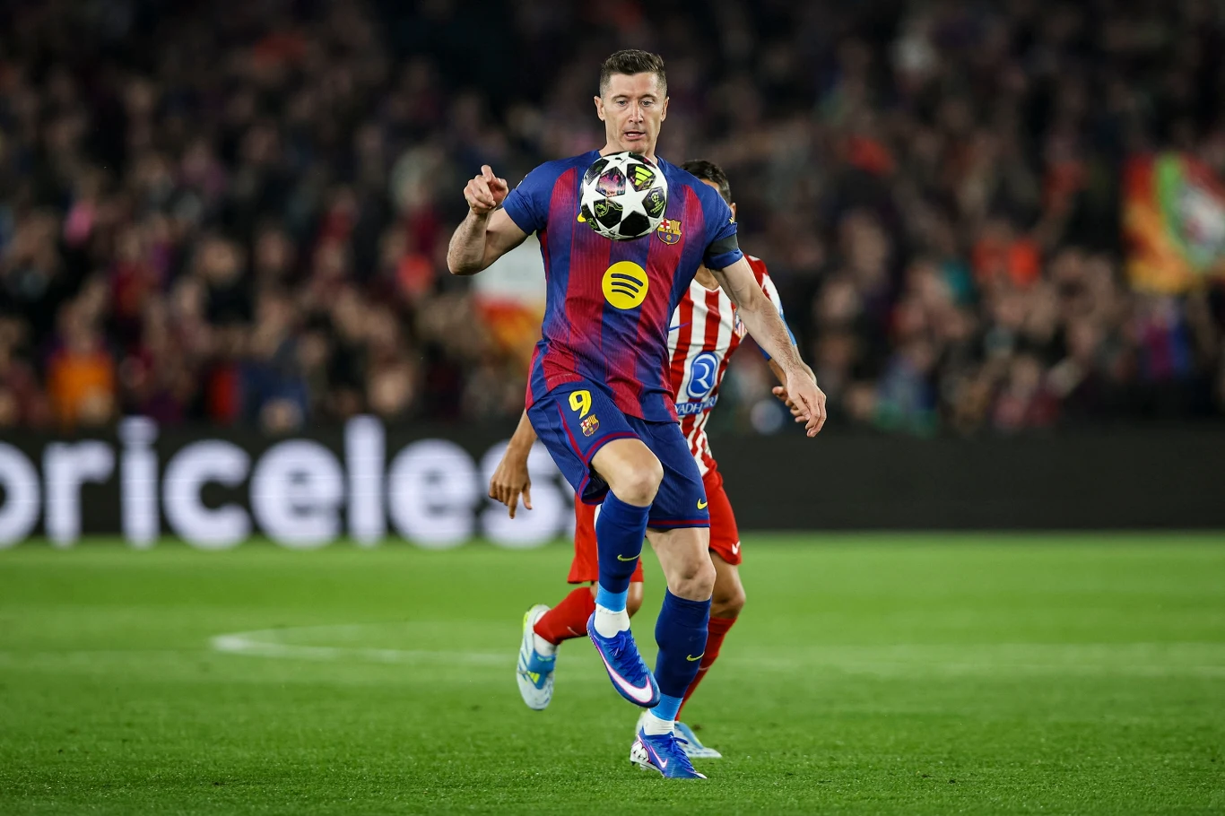 Piłkarz FC Barcelony w bordowo-granatowym stroju z numerem 9 wykonuje techniczne zagranie podczas meczu, podskakując i kontrolując piłkę, w tle widoczny zawodnik drużyny przeciwnej w czerwono-białych pasach oraz kibice na trybunach.