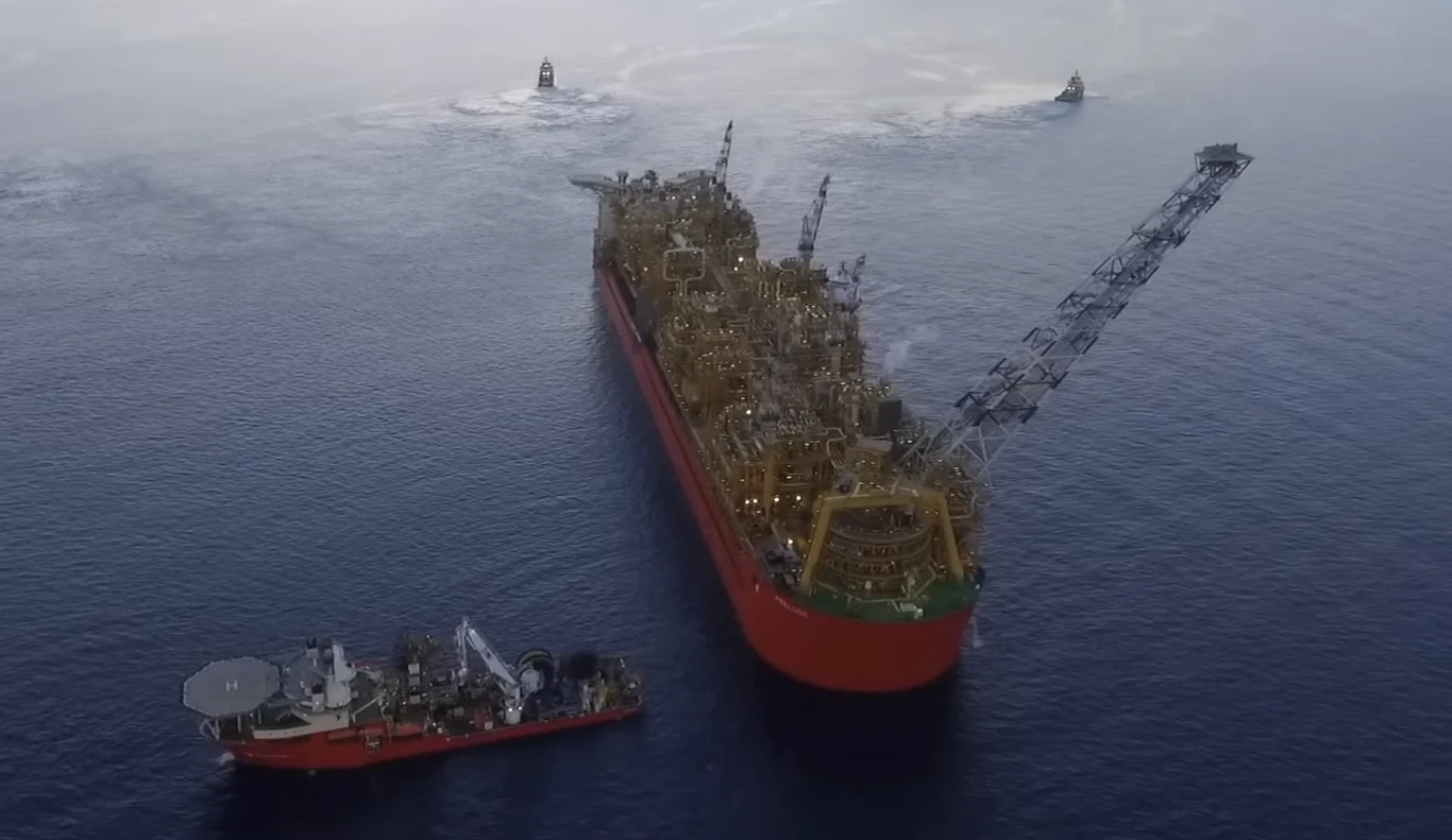 Prelude FNLG jest w stanie wytrzymać huragany 5. kategorii. duża platforma wydobywcza typu FPSO na otwartym morzu z towarzyszącym jej statkiem serwisowym oraz dwoma mniejszymi jednostkami na dalszym planie, całość otoczona spokojnymi wodami oceanu