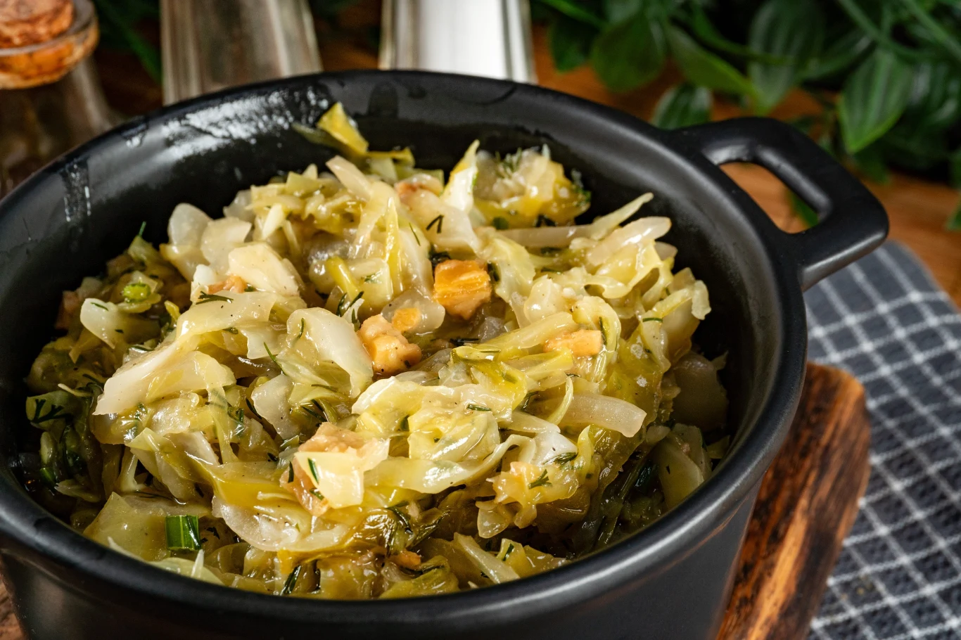 Bezglutenowy zagęszczacz do młodej kapusty. Wychodzi lekka i aksamitna Bezglutenowa młoda kapusta duszona z koperkiem i skwarkami, podana w czarnym garnku na desce, przyprawy w tle
