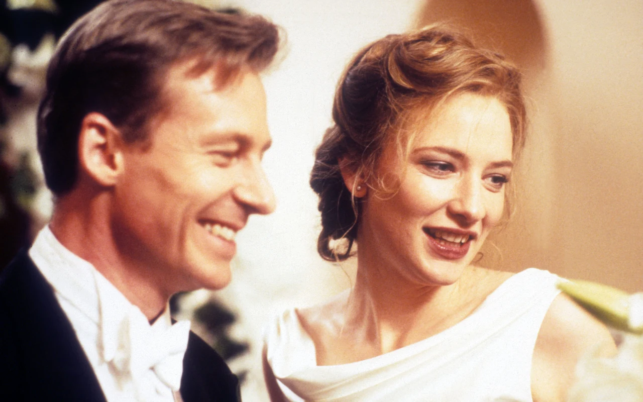 uśmiechnięta para w eleganckich strojach, kobieta ma na sobie białą suknię z odkrytymi ramionami, a mężczyzna smoking i białą muchę, oboje wyglądają na szczęśliwych, tło rozmyte z jasnymi dekoracjami