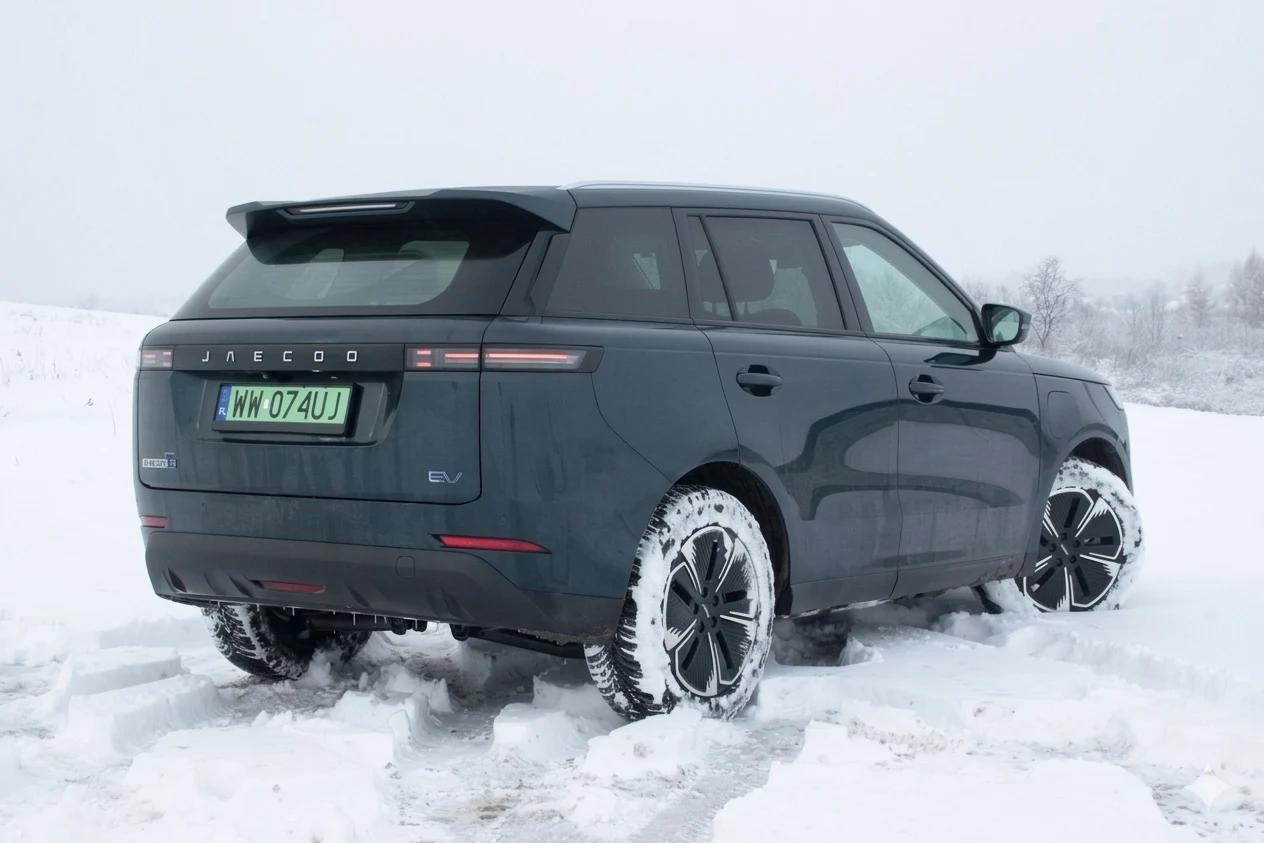 ciemnoszary SUV z napędem elektrycznym na śnieżnej drodze, pokryty śniegiem wokół kół, z wyraźnymi numerami rejestracyjnymi oraz charakterystycznym jednolitym pasem tylnych świateł