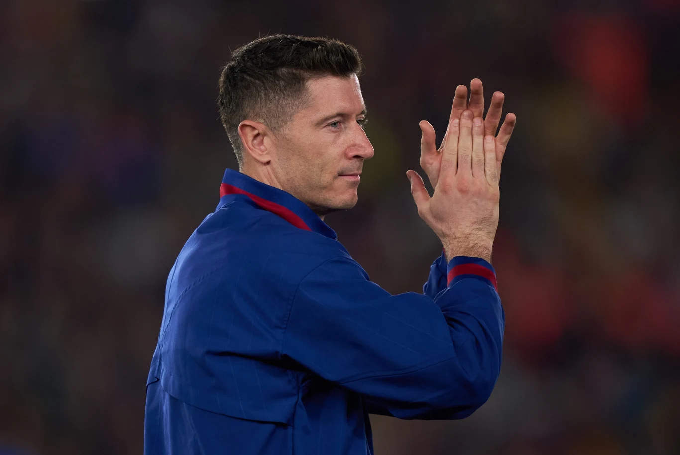 Robert Lewandowski Robert Lewandowski w niebieskiej kurtce stoi bokiem i klaszcze na tle stadionu pełnego kibiców