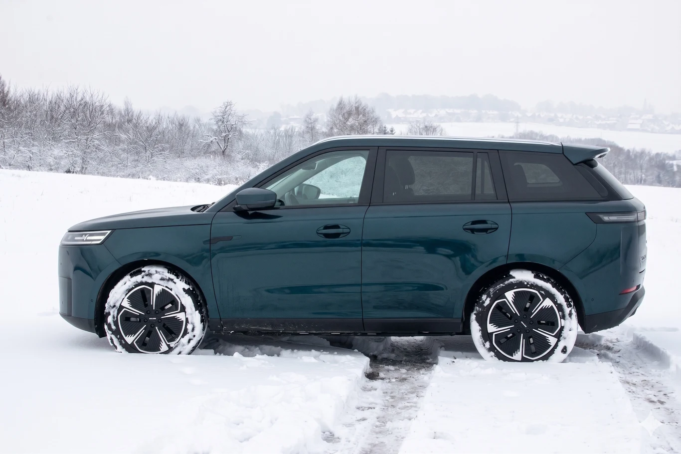 ciemnozielony SUV stoi na ośnieżonej drodze, wokół rozciąga się zimowy krajobraz z pokrytymi śniegiem polami i drzewami