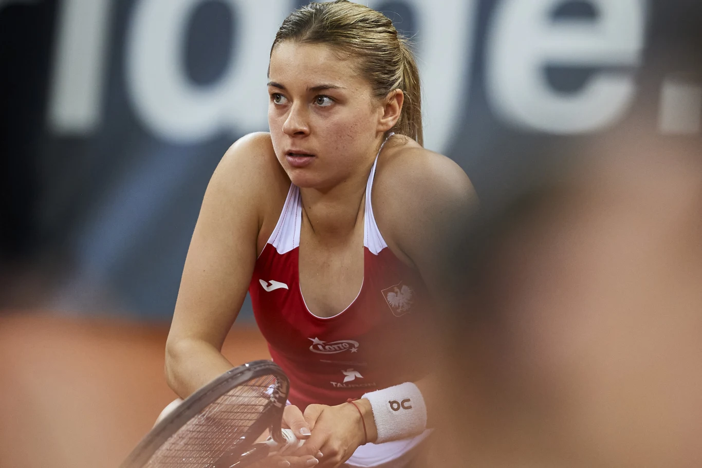kobieta w stroju sportowym z logo Polski trzymająca rakietę tenisową, skoncentrowana i skupiona przed meczem