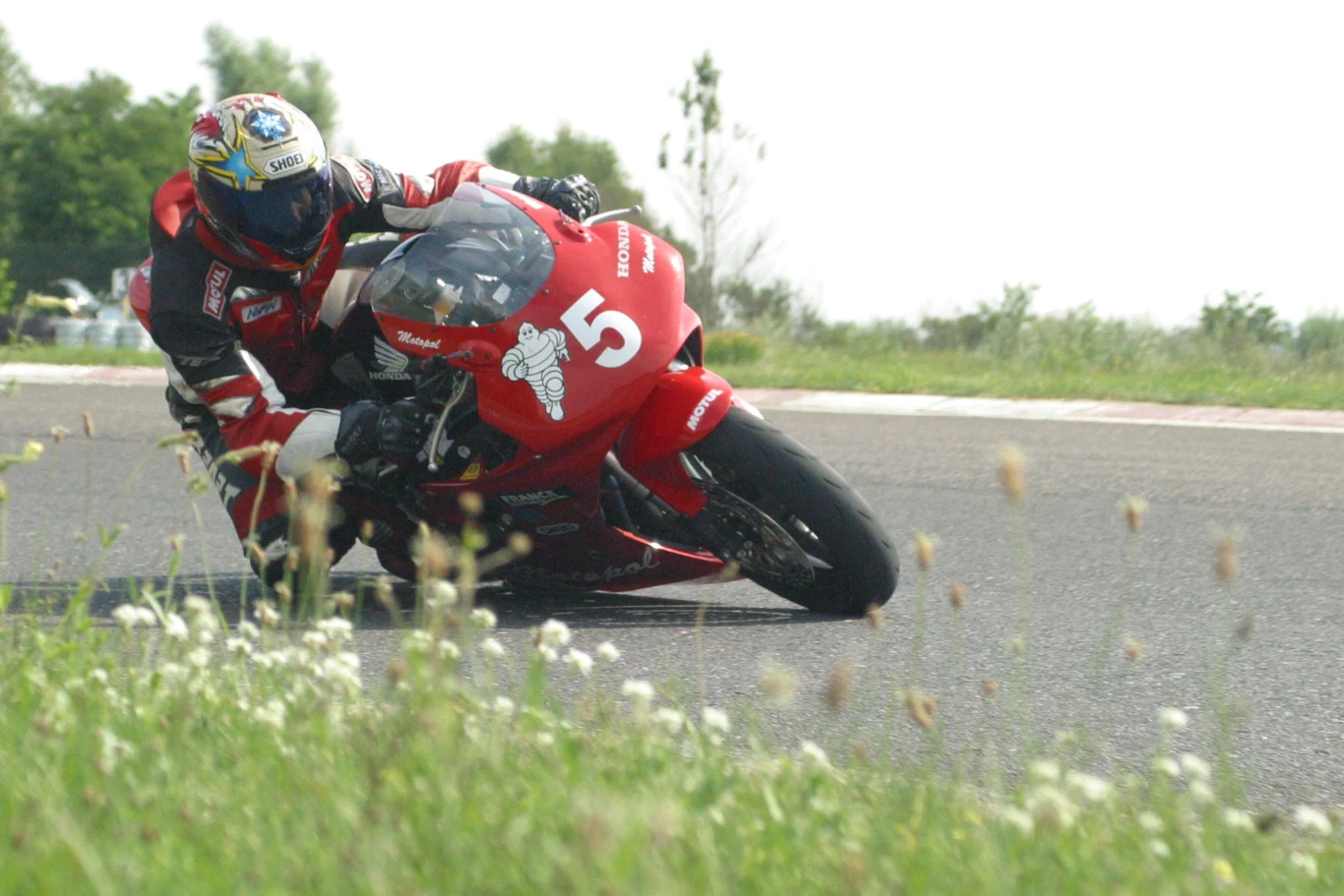 Tor Poznań to jedyne miejsce w Polsce, gdzie odbywają się duże zawody motocyklowe i samochodowe motocyklista w wyścigowym kombinezonie pochylony na czerwonym sportowym motocyklu z numerem 5, pokonujący zakręt na torze asfaltowym