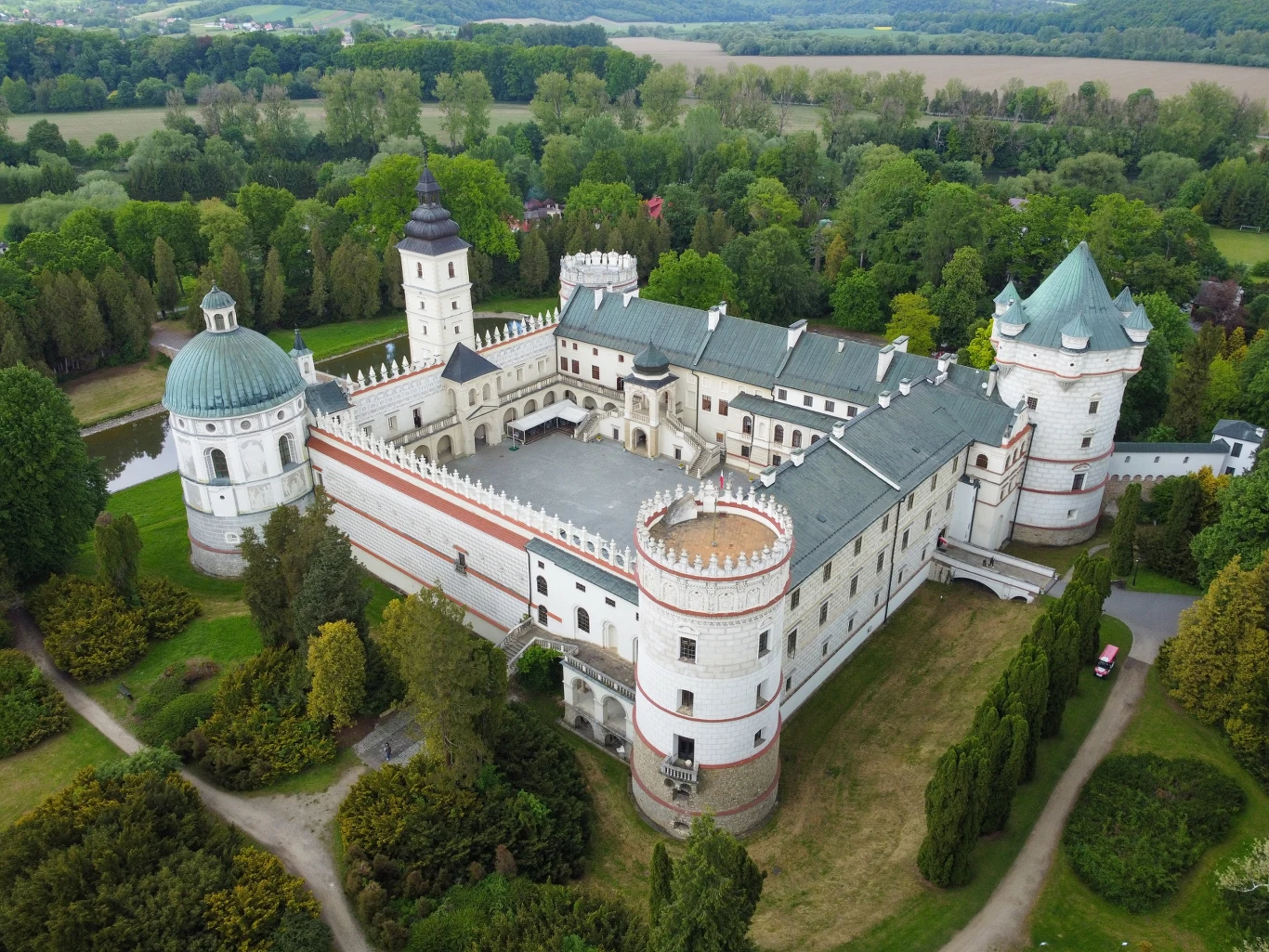 rozległy renesansowy zamek otoczony murami i wieżami, z charakterystyczną cylindryczną basztą narożną oraz białą kaplicą z kopułą, położony wśród zieleni i parku, z centralnym dziedzińcem i widoczną wieżą zegarową