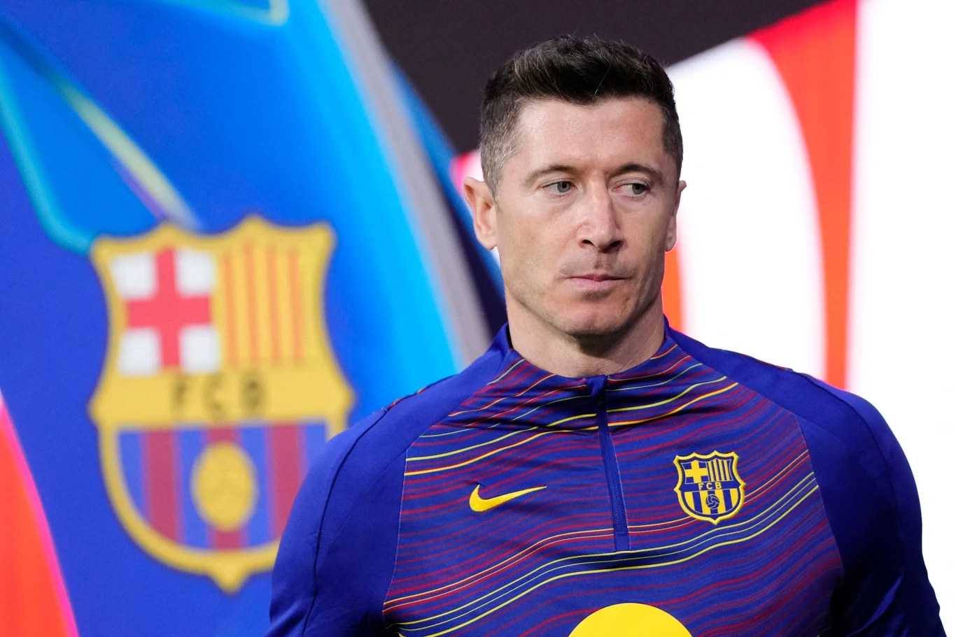 Robert Lewandowski Robert Lewandowski w koszulce FC Barcelony stoi na tle dużego herbu klubowego, patrzy lekko w bok