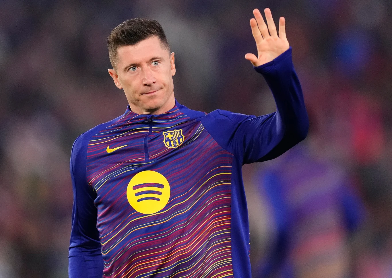 Robert Lewandowski, 08.04.2026 r. Robert Lewandowski, 8.04.2026, w rozgrzewkowej bluzie FC Barcelona, unosi rękę na rozmytym tle