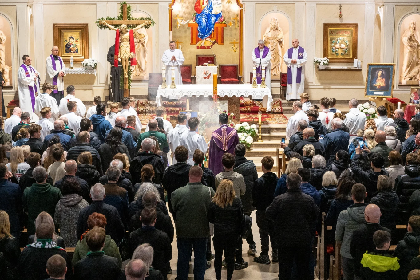 Msza święta w kościele, kapłani i ministranci przy ołtarzu w obecności licznie zgromadzonych wiernych, ołtarz udekorowany kwiatami i liturgicznymi szatami, w centrum figura Chrystusa Zmartwychwstałego podwieszona nad ołtarzem.