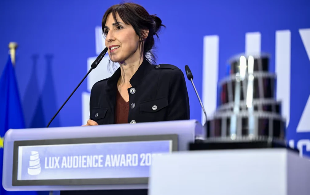 Eva Libertad, autorka filmu "Deaf", z nagrodą LUX, fot. Parlament Europejski Eva Libertad przy mównicy z mikrofonem, obok statuetka LUX, fragment flagi i logo wydarzenia w tle