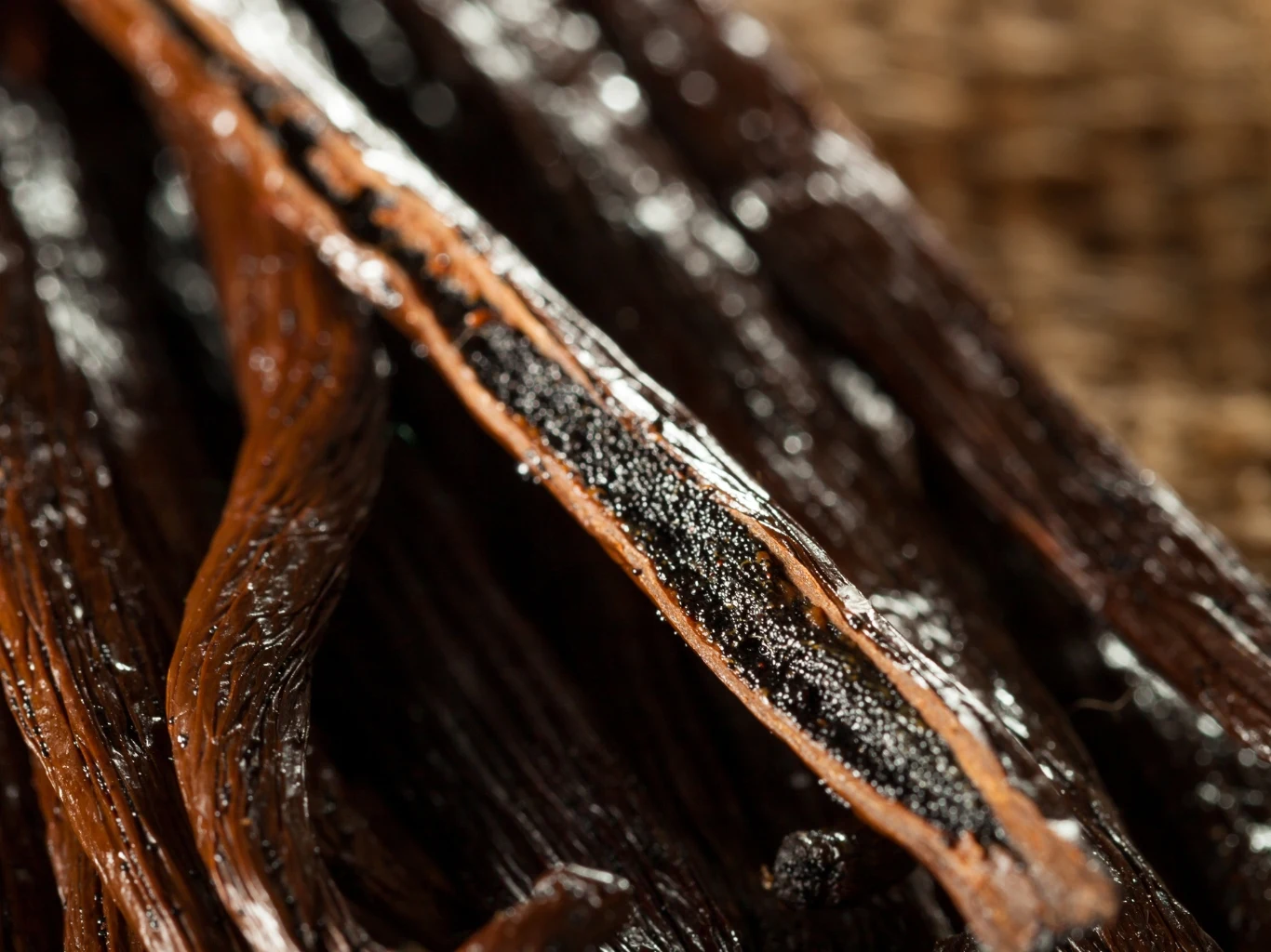 Te ziarenka nie tylko zmieniają smak, ale dodają prozdrowotnych właściwości potrawom. Laski wanilii przekrojone wzdłuż z widocznymi czarnymi ziarenkami na wilgotnej powierzchni.