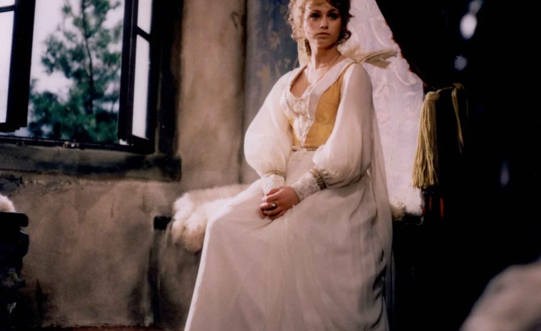 Kadr z serialu "Arabela", fot. Timeless Film Festival Warsaw młoda kobieta w długiej, jasnej sukni z bufkami siedzi na ławie przy oknie w przytulnym, lekko zniszczonym wnętrzu o miękkim świetle
