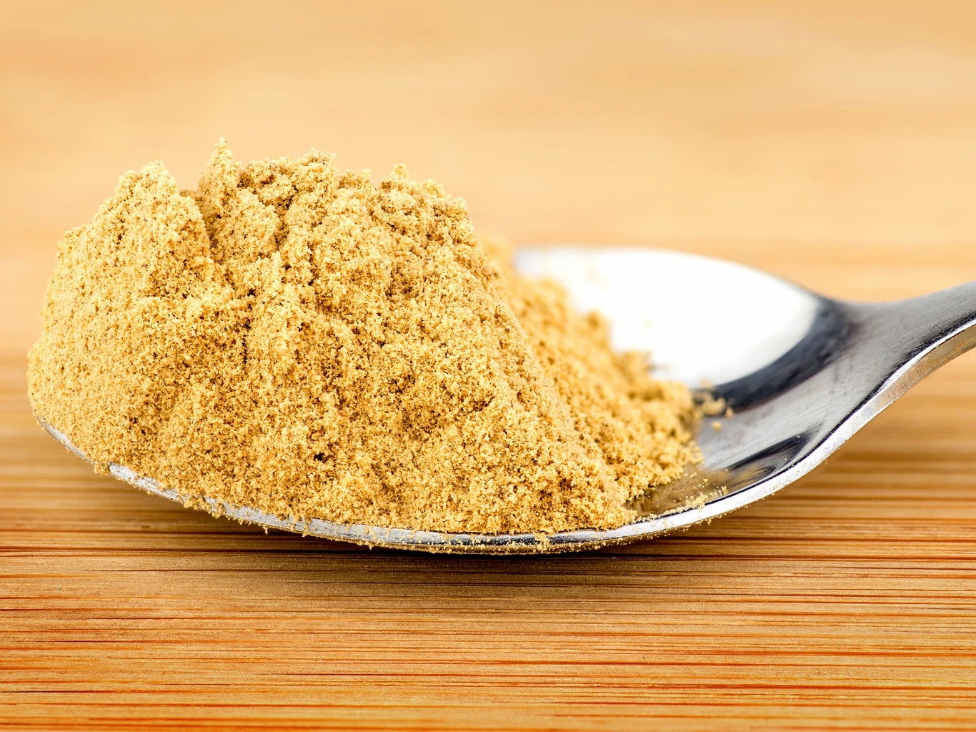 Czy imbir w proszku jest zdrowy? Kto powinien go spożywać? Srebrna łyżeczka z jasnożółtym imbirem w proszku leży na drewnianym blacie.