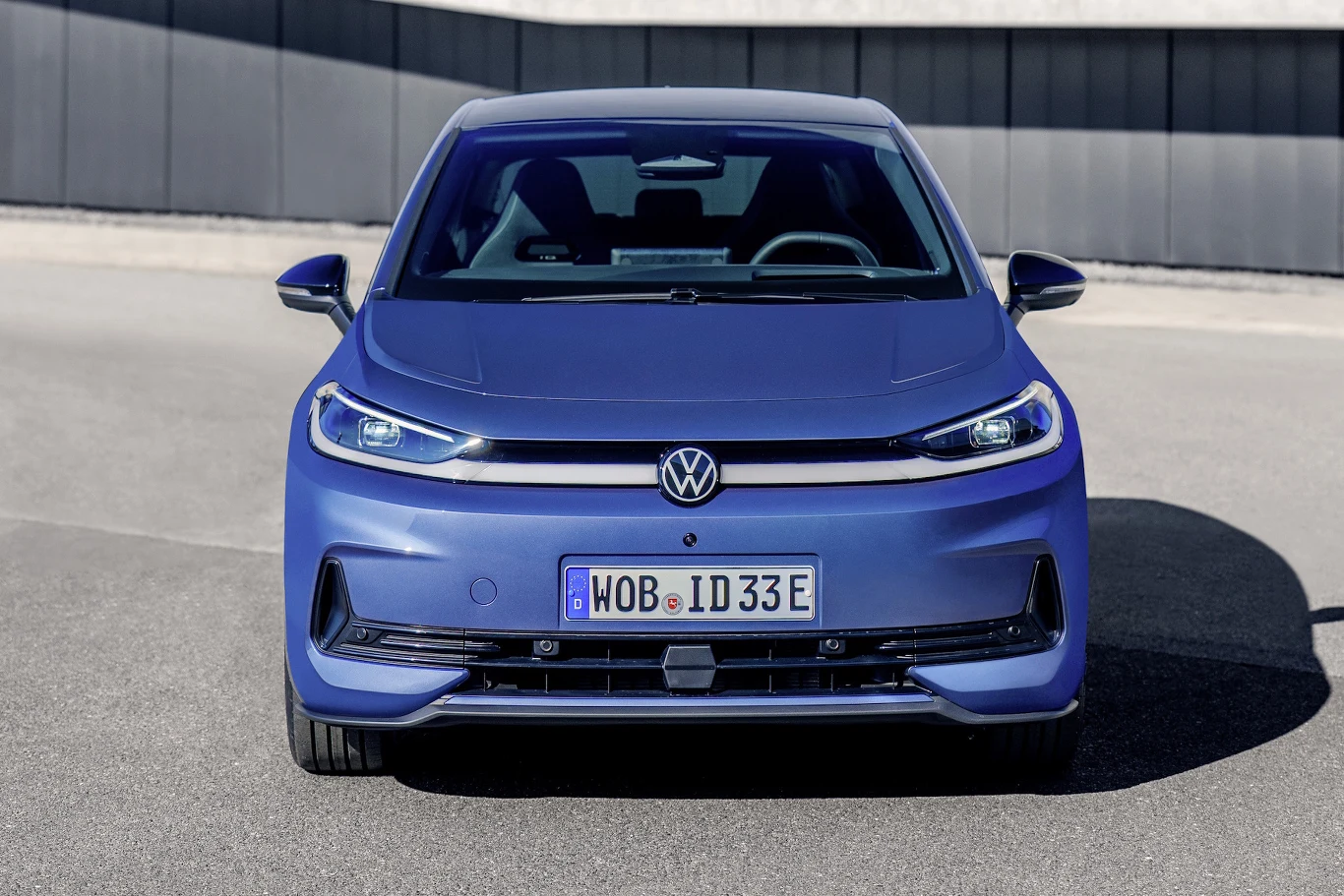 niebieski samochód osobowy marki Volkswagen, model ID.3, widoczny z przodu, charakterystyczne światła LED, logo VW na środku maski, nowoczesny design nadwozia