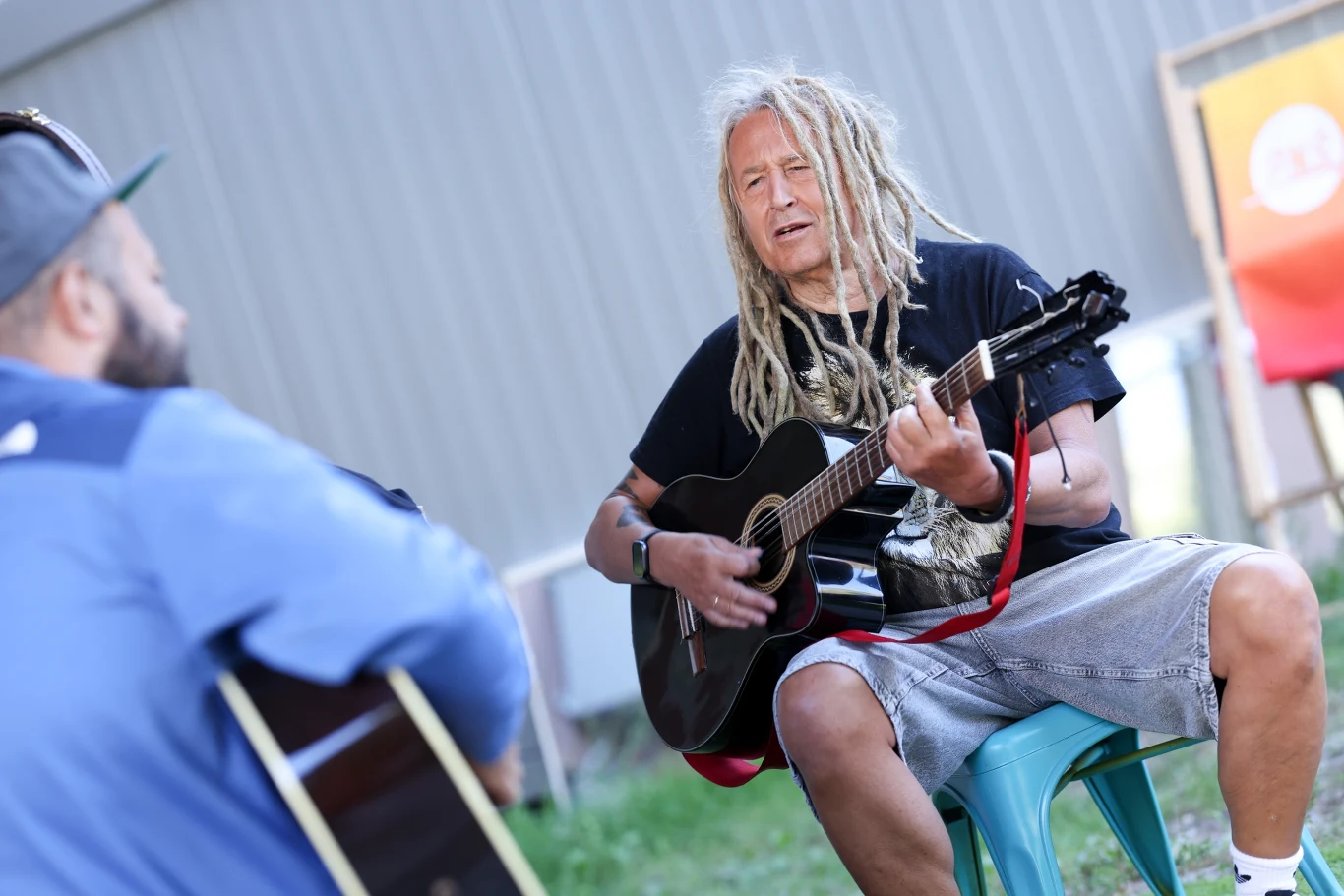 Darek "Maleo" Malejonek z powodu choroby odwołał najbliższe koncerty, tyłem gitarzysta Kuba Leciej Darek "Maleo" Malejonek z gitarą akustyczną, obok gitarzysta Kuba Leciej, w tle metalowa ściana i plakat