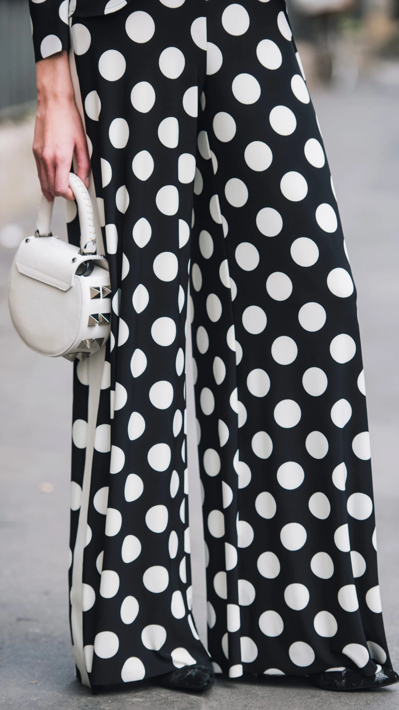 Czarne, szerokie spodnie w białe grochy, trzymana w lewej dłoni mała, biała torebka o zaokrąglonym kształcie.