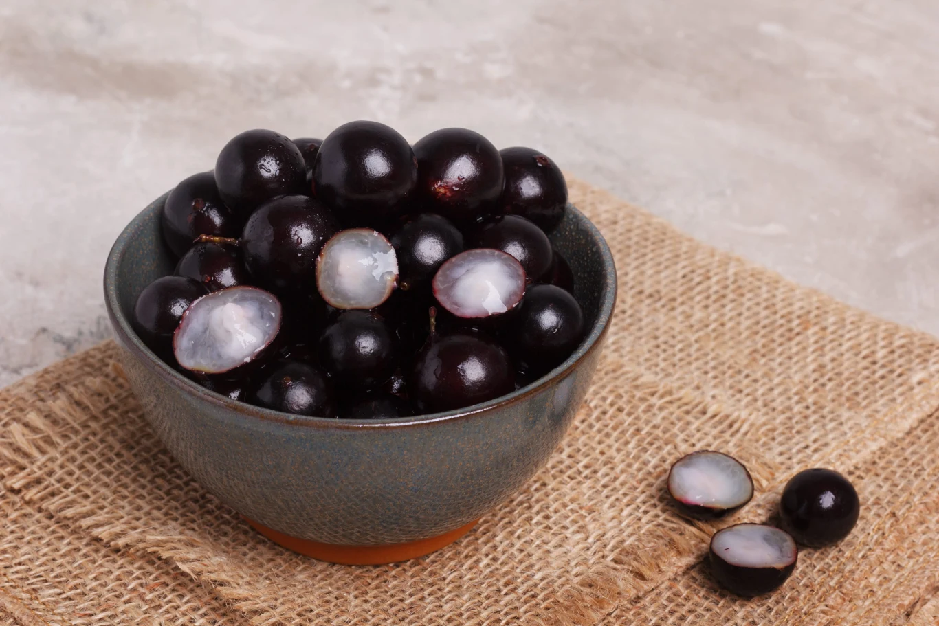 Jamun barwi język na fioletowo fioletowo-czarne jagody jabuticaba w misce na jutowym materiale, niektóre owoce przekrojone na pół ukazują jasny, soczysty miąższ