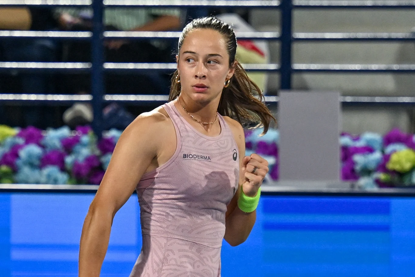 tenisistka w sportowej sukience z opaską na nadgarstku, skupiona podczas meczu na korcie, w tle trybuny z kibicami oraz dekoracyjne kwiaty