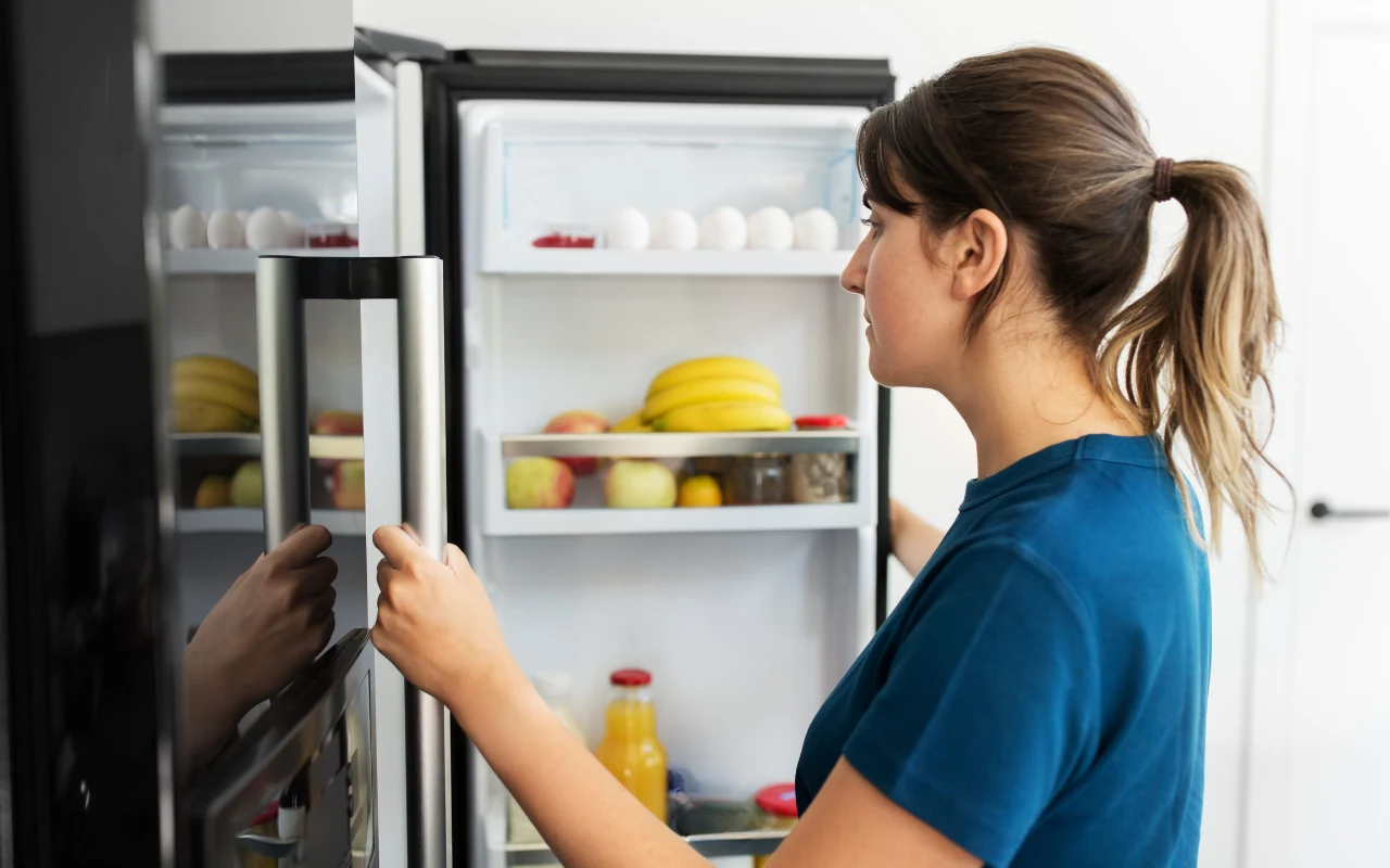 Co na kolację bez chleba? 5 pomysłów na szybkie dania z tego, co masz w domu Kobieta w granatowej koszulce zagląda do lodówki, zastanawia się co ugotować na kolację