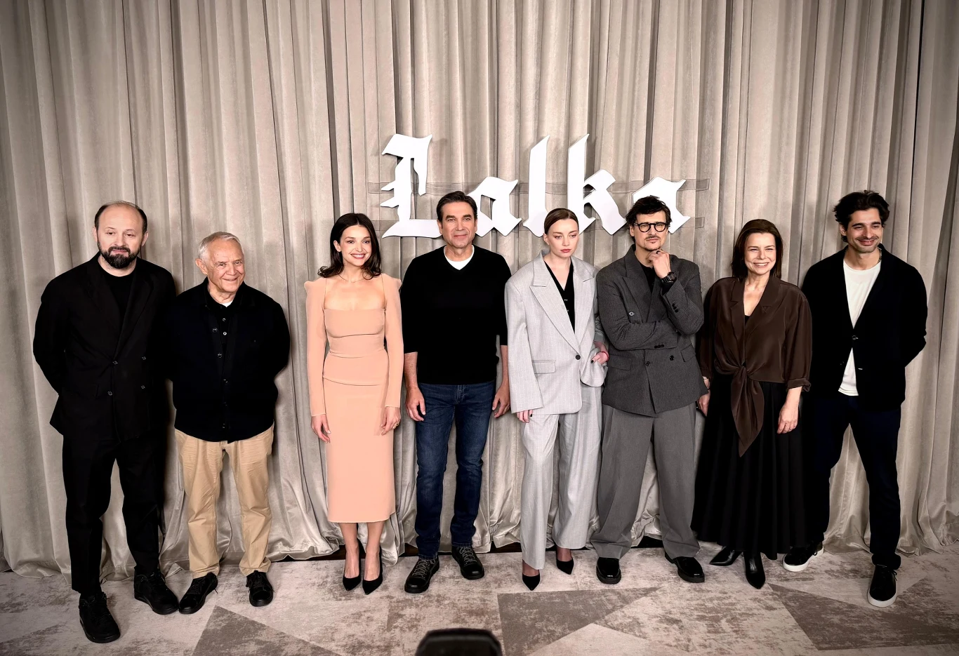 Dzień prasowy filmu "Lalka" Osiem osób pozuje wspólnie przed jasną kotarą, na której widnieje napis „Lalka”; centralne miejsce zajmują kobieta w jasnym, dopasowanym kostiumie oraz mężczyzna w ciemnym swetrze, po bokach stoją inni członkowie grupy ubrani w różnorodne stroje – od e...