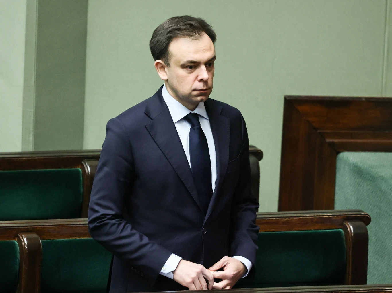 Minister finansów Andrzej Domański Andrzej Domański w granatowym garniturze i białej koszuli stoi w ławie sejmowej, w tle sala obrad