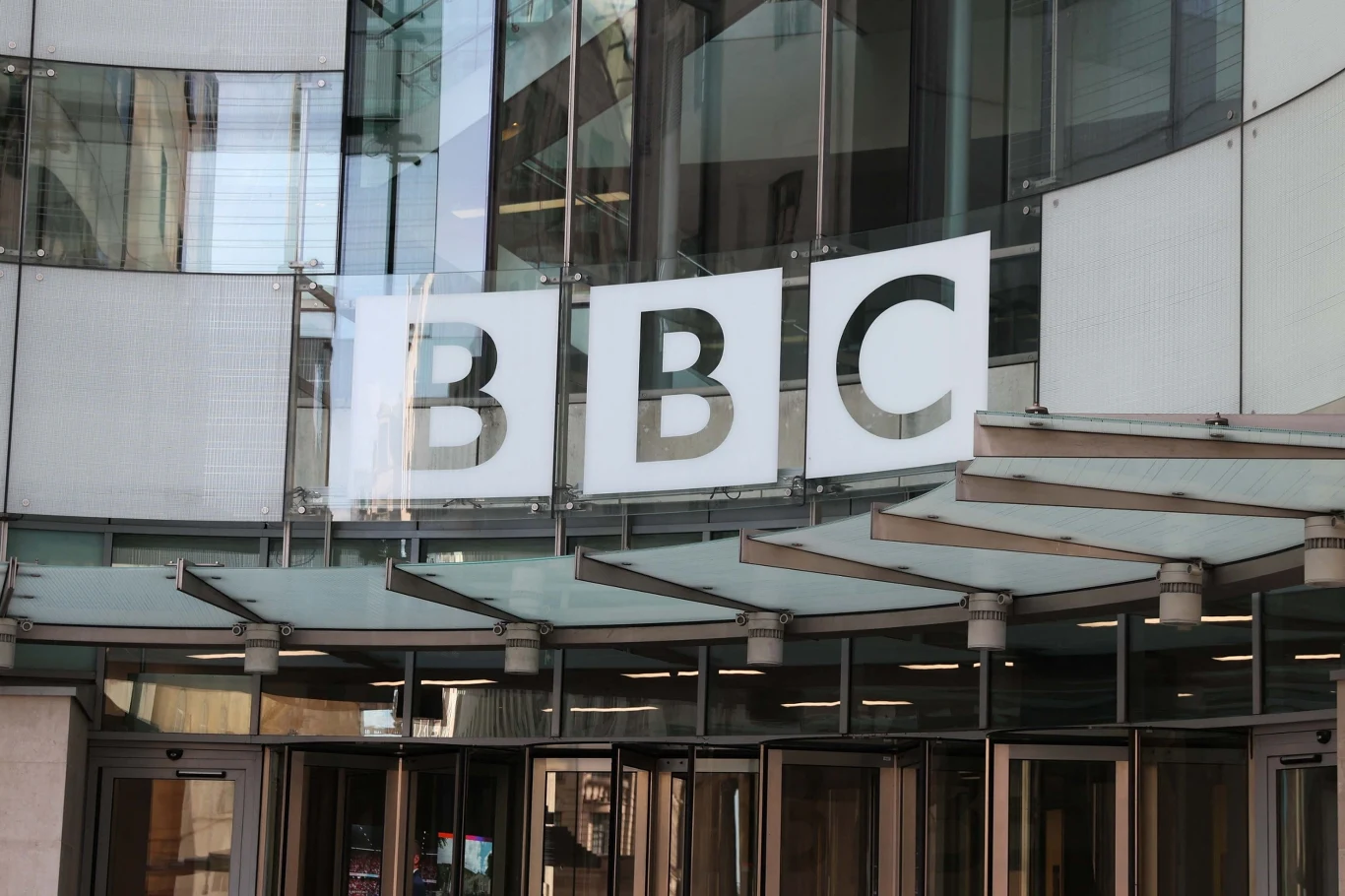 BBC planuje zwolnić do dwóch tysięcy pracowników w ciągu dwóch lat Logo BBC na szklanej fasadzie nowoczesnego budynku nad przeszklonymi drzwiami wejściowymi.
