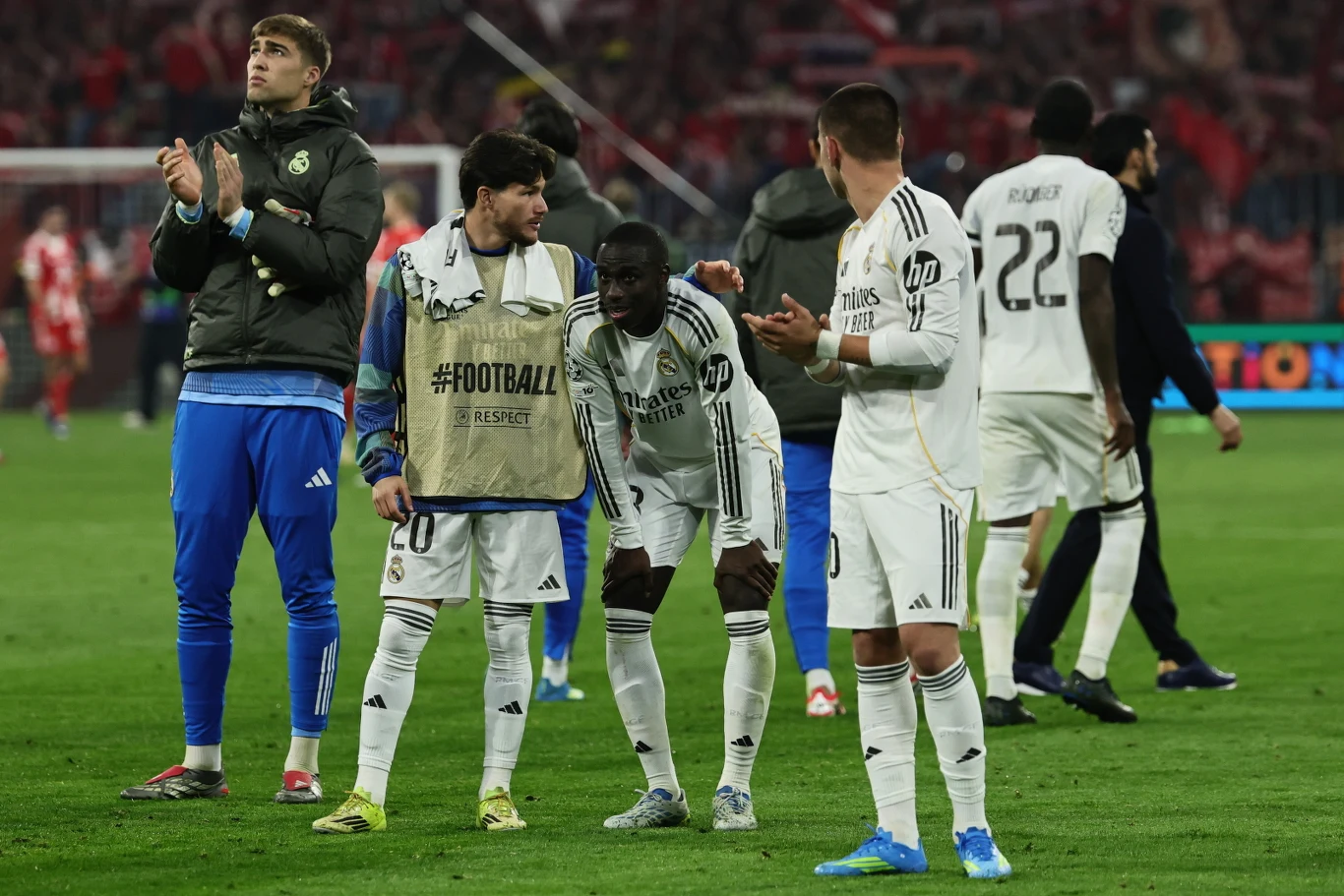 grupa piłkarzy w białych strojach stoi na murawie stadionu, kilku z nich klaszcze, jeden zawodnik pochyla się lekko do przodu, atmosfera skupienia i oczekiwania, w tle widoczne trybuny z kibicami