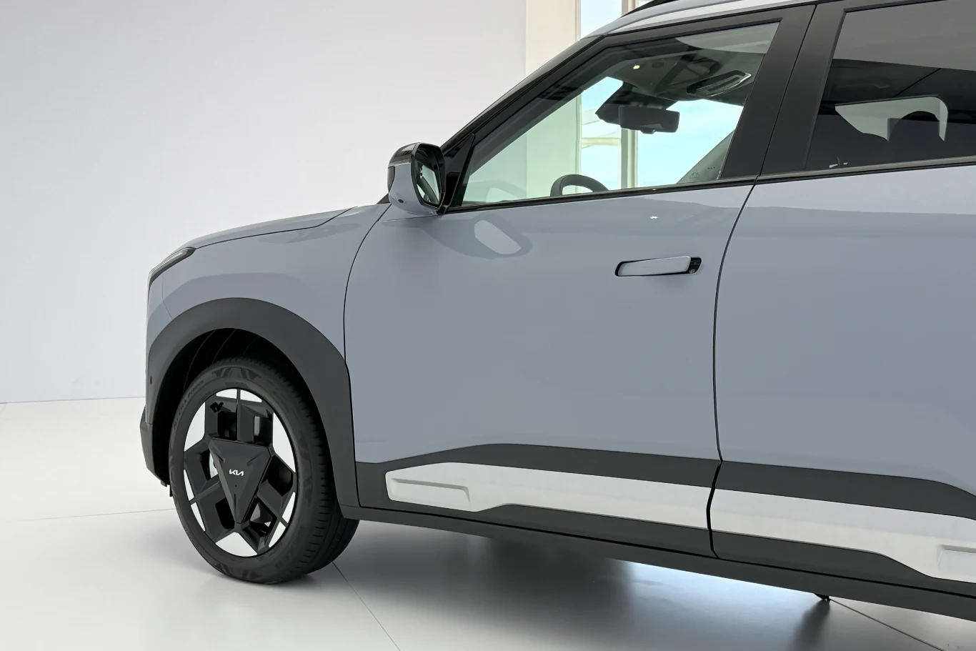 nowoczesny samochód SUV w jasnoszarym kolorze, z czarnymi wstawkami i designerskimi, pięcioramiennymi felgami, prezentowany w minimalistycznym, jasnym wnętrzu