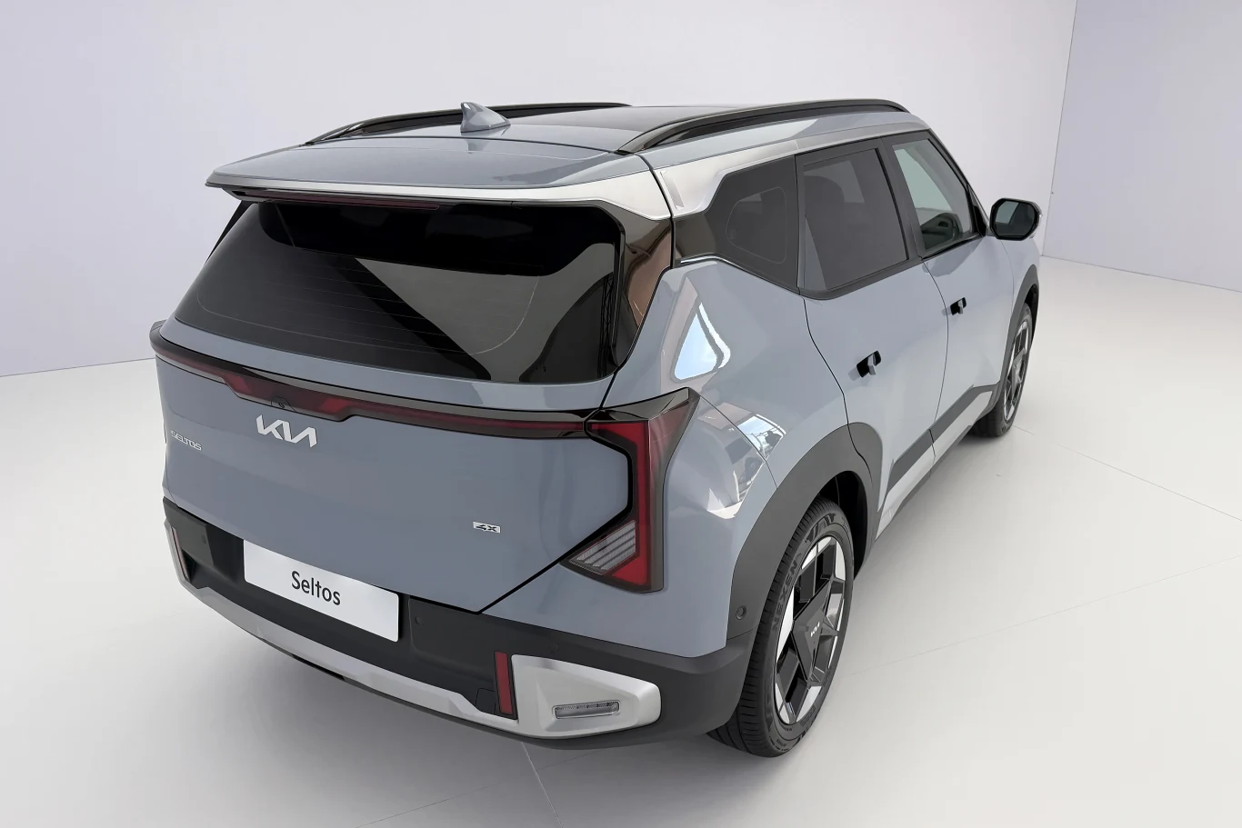 Nowoczesny SUV Kia Seltos w szarym kolorze o dynamicznej sylwetce, z charakterystycznymi tylnymi światłami LED w kształcie litery T oraz czarnym dachem optycznie oddzielonym od reszty nadwozia.