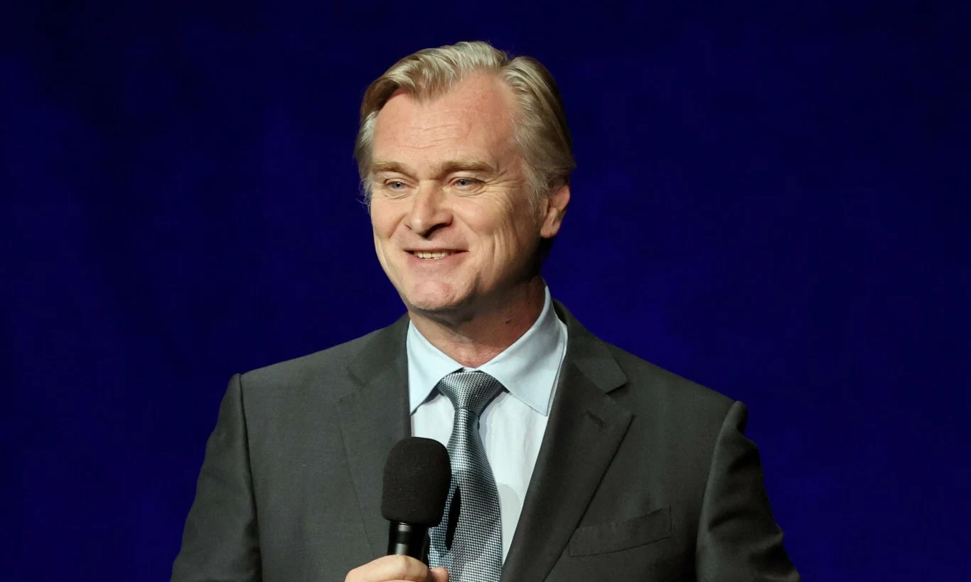 Christopher Nolan Christopher Nolan w garniturze z jasnoniebieskim krawatem, trzyma mikrofon na tle granatowego tła