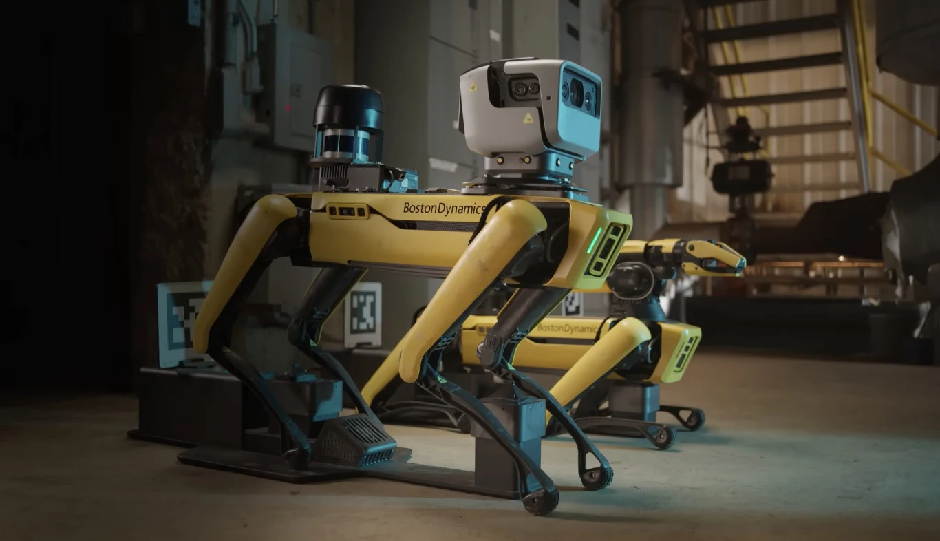 Robopies Spot z Google Gemini. Boston Dynamics chwali się udoskonaleniami. Dwa żółto-czarne roboty Spot Boston Dynamics z czujnikami i kamerami na przemysłowej podłodze, schody w tle