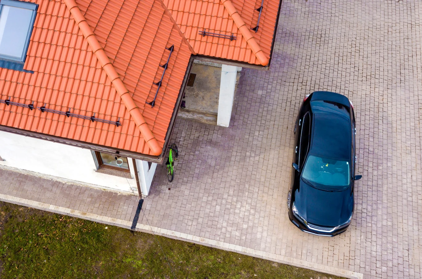 Dopłata do wiaty samochodowej. 23 tys. zł, ale trzeba się spieszyć. Czarny samochód na kostce brukowej obok nowoczesnego domu z czerwonym dachem i zielonym rowerem przy ścianie